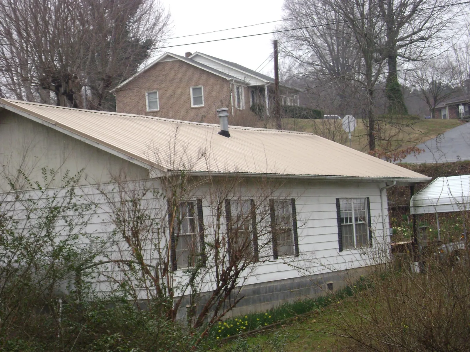 Tan metal roof on a white sided house set into a hillside — Commercial Roofing by Roofing Brothers in Atlantic City